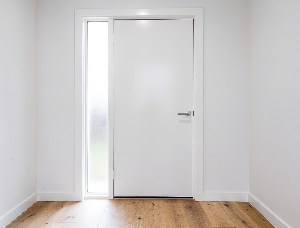 Freshly painted white front door with chrome lever handle, frosted sidelight and white architrave in an Aintree new build