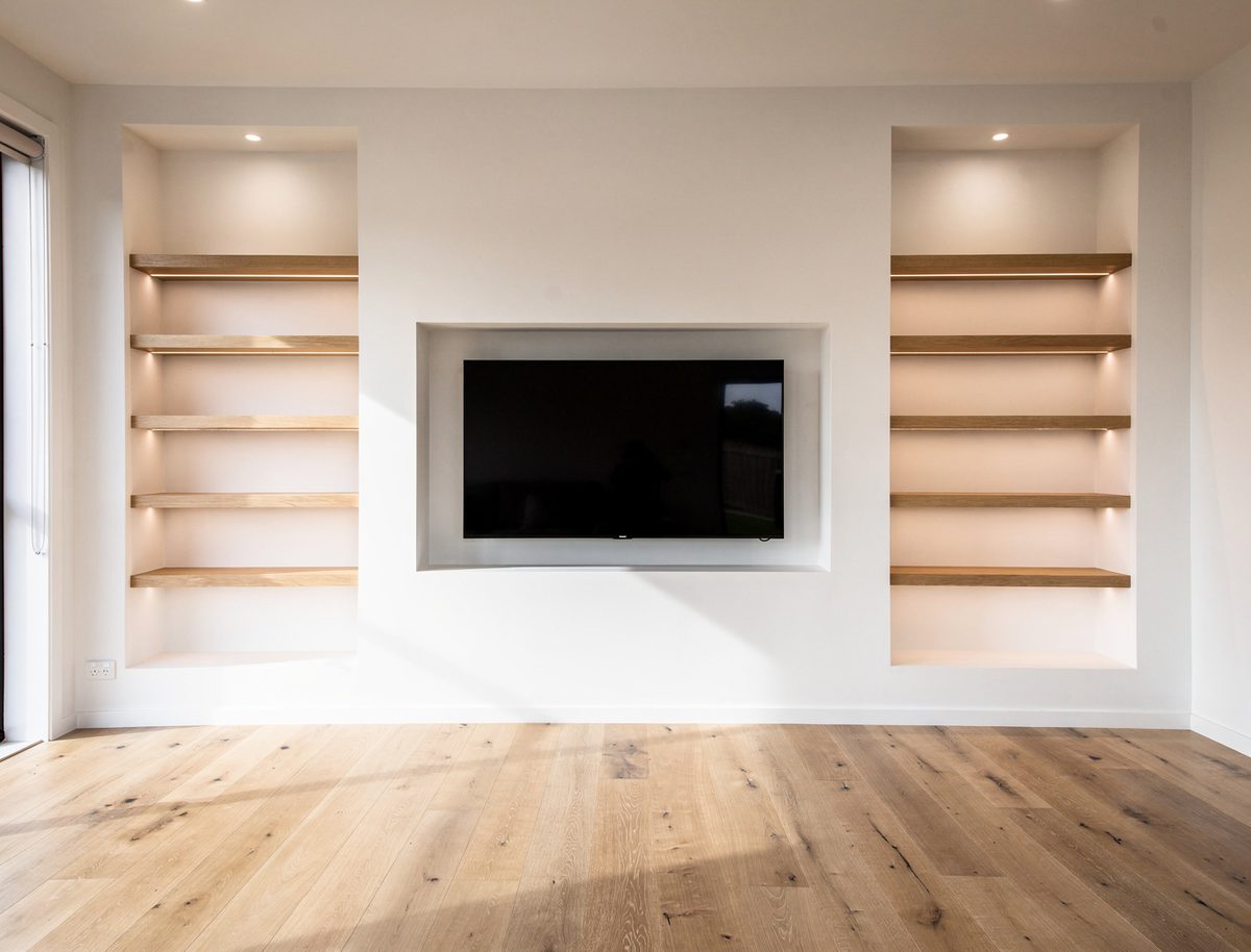 Built-in entertainment unit with empty oak floating shelves against freshly painted white walls in an Aintree living room