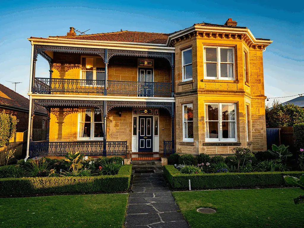 Grand Victorian Italianate double-storey sandstone home in Essendon with ornate navy cast iron lacework, stained glass transoms, two-storey bay window and terracotta tile roof