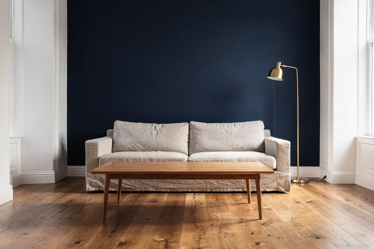 Living room with deep navy blue feature wall, natural linen sofa, timber coffee table and brass floor lamp in a renovated Williamstown home